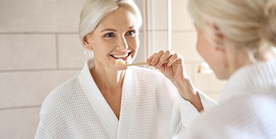 Woman smiling while brushing her teeth in bathroom