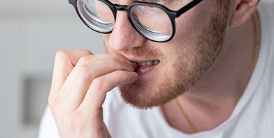 Man with black glasses biting his nails